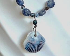 Closeup of blue sodalite beads and ceramic shell pendant. The pendant has blue and brown vertical ridges.